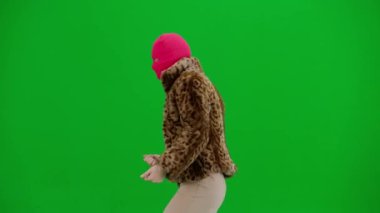 Pembe kar maskeli kadın, kaplan kürkü manto ve gece elbisesi giyip neşeyle dans ediyor. Stüdyoda yeşil arka plandaki kadın ucubesi. Moda eğilimi kavramı, feminist moda eğilimi