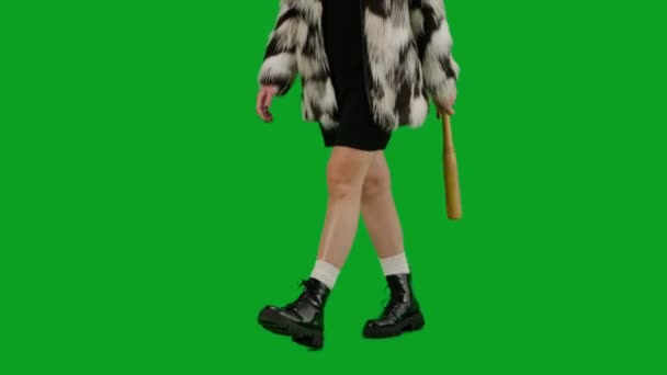 穿着毛皮外套和晚礼服的女人手拿着球棒走路 工作室里的女性对绿色背景非常好奇 时尚潮流理念 女权主义潮流在时尚半圈 — 图库视频影像