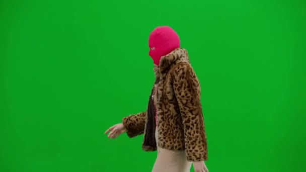 身穿粉色巴拉克拉瓦 虎皮大衣和晚礼服的女人走路 工作室里的女性对绿色背景非常好奇 时尚潮流的概念 时尚方面的女性主义趋势 — 图库视频影像