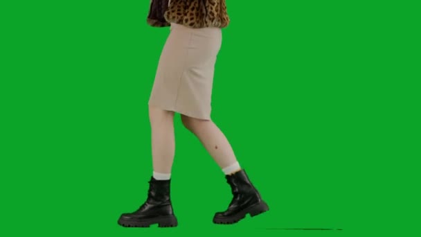 穿着毛皮外套和晚礼服的女人手拿着球棒走路 工作室里的女性对绿色背景非常好奇 时尚潮流的概念 时尚方面的女性主义趋势 — 图库视频影像