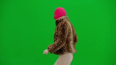 Pembe kar maskeli kadın, kaplan kürkü ve gece elbisesi giyen dans eden ve işaret parmağını farklı yönlere çeviren kadın. Stüdyo manzaralı yeşil arka planda ucube bir kadın.