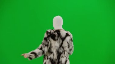 Beyaz kar maskeli kadın, palto ve gece elbisesi giyen dans eden ve işaret parmağını farklı yönlere çeviren kadın. Stüdyonun arka planında yeşil arka planda ucube bir kadın var.