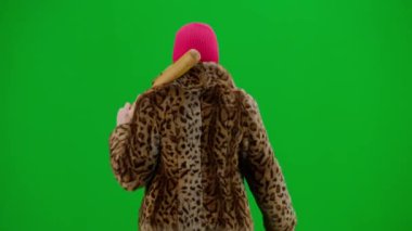 Pembe kar maskeli kadın, kaplan kürkü manto ve elinde yarasayla yürüyen gece elbisesi. Stüdyoda yeşil arka plandaki kadın ucubesi. Moda eğilimi kavramı, feminist moda eğilimi