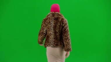 Pembe kar maskeli kadın, kaplan kürkü manto ve gece elbisesi yürüyüşü. Stüdyoda yeşil arka plandaki kadın ucubesi. Moda eğilimi kavramı, feminist moda eğilimi
