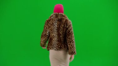 Pembe kar maskeli kadın, kaplan kürkü manto ve gece elbisesi yürüyüşü. Stüdyoda yeşil arka plandaki kadın ucubesi. Moda eğilimi kavramı, feminist moda eğilimi