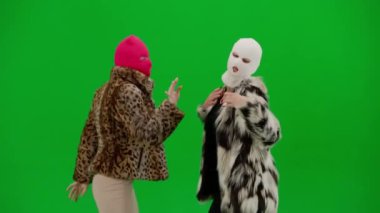 Beyaz ve pembe kar maskeli iki kadın kamera önünde model gibi poz veriyor. Stüdyoda yeşil arka planda kürklü kadınlar. Moda eğilimi, feminist moda eğilimi