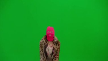 Pembe kar maskeli kadın, kaplan ceketli ve gece elbisesi sallanan ve kollarını sallayan. Stüdyoda yeşil arka plandaki ucube kadın. Moda eğilimi, feminist moda eğilimi