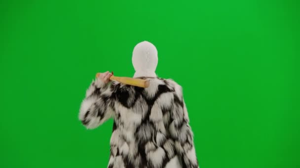 身穿白色巴拉克拉法帽 皮大衣和晚礼服的女人手拿着球棒走着 工作室里的女性对绿色背景非常好奇 时尚潮流的概念 时尚后视镜中的女性主义趋势 — 图库视频影像