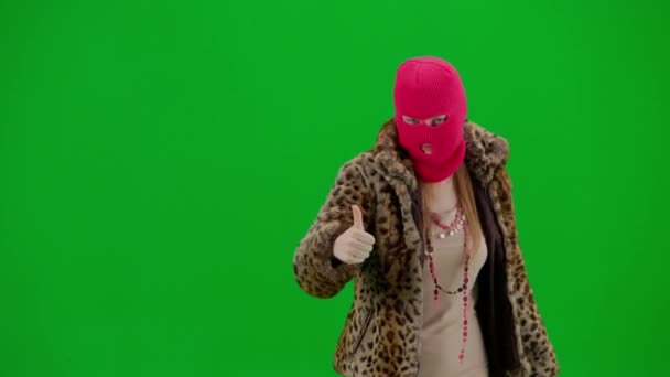 身穿粉色巴拉克拉法帽 虎皮大衣和晚礼服的女人把手指指向旁边 展示了一个竖起大拇指的姿势 工作室里一个绿色背景的怪胎女人 — 图库视频影像