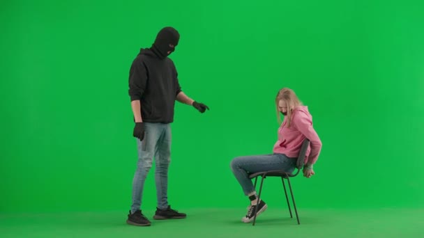 抢劫和犯罪概念 色键绿色屏幕背景上的小偷和受害者的肖像 女孩坐在椅子上捆着双手 用枪威胁着她 把嘴塞得紧紧的 — 图库视频影像