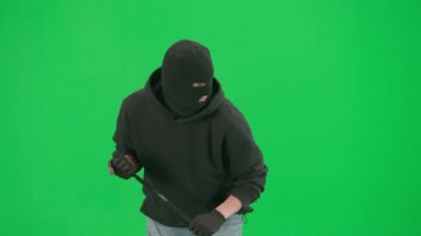 Soygun ve ceza konsepti. Krom anahtar yeşil ekrandaki hırsızın portresi. Kar maskeli ve kapüşonlu bir adam elinde levyeyle yürüyüp etrafa bakıyor..