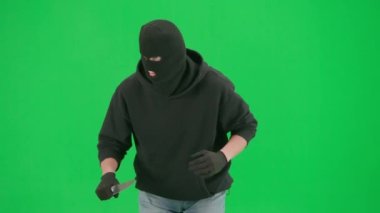 Soygun ve ceza konsepti. Krom anahtar yeşil ekrandaki hırsızın portresi. Kar maskeli ve kapüşonlu bir adam elinde bıçakla dolaşıyor. Etrafa bakıyor..