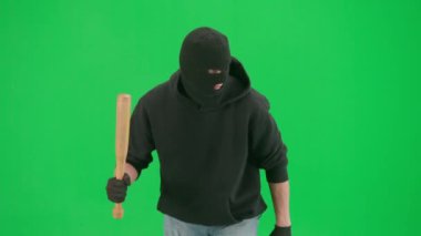 Soygun ve ceza konsepti. Krom anahtar yeşil ekrandaki hırsızın portresi. Kar maskeli ve kapüşonlu bir adam elinde beyzbol sopasıyla yürüyüp etrafa bakıyor..
