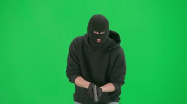 Soygun ve ceza konsepti. Krom anahtar yeşil ekrandaki hırsızın portresi. Kar maskeli ve kapüşonlu bir adam elinde silahla dolaşıyor. Etrafa bakıyor..
