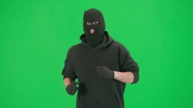 Soygun ve ceza konsepti. Krom anahtar yeşil ekrandaki hırsızın portresi. Kapüşonlu, kot pantolonlu ve kar maskeli bir adam suç işlemeye hazırlanıyor..