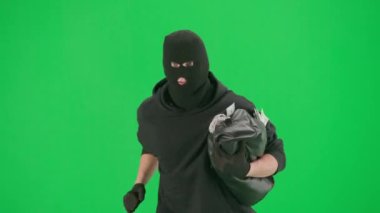 Soygun ve ceza konsepti. Krom anahtar yeşil ekrandaki hırsızın portresi. Kapüşonlu, kot pantolonlu ve kar maskeli bir adam, çalıntı çanta dolusu parayla polisten kaçıyor..