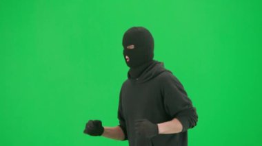 Soygun ve ceza konsepti. Krom anahtar yeşil ekrandaki hırsızın portresi. Kapüşonlu, kot pantolonlu ve kar maskeli bir adam suç işlemeye hazırlanıyor. Yarım dönüş.
