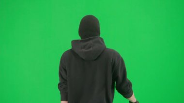 Soygun ve ceza konsepti. Krom anahtar yeşil ekrandaki hırsızın portresi. Kapüşonlu, kot pantolonlu ve kar maskeli bir adam suç işlemeye hazırlanıyor. Arka plan