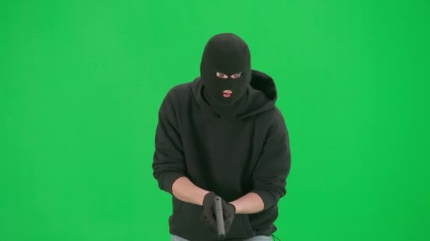 強盗と犯罪概念 クロマキーグリーンの背景に泥棒の肖像画 バラカバラの男強盗とフーディーウォーキング 手で銃を持って周りを見回す — ストック動画