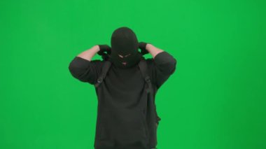 Soygun ve ceza konsepti. Krom anahtar yeşil ekrandaki hırsızın portresi. Kar maskesi takan, silahını kontrol eden, sırt çantasını tamir eden ve suç işlemeye hazırlanan bir adam..