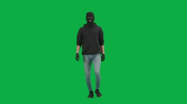 Soygun ve ceza konsepti. Krom anahtar yeşil ekrandaki hırsızın portresi. Kapüşonlu, kot pantolonlu ve kar maskeli bir adam suç işlemeye hazırlanıyor..