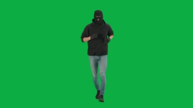 Soygun ve ceza konsepti. Krom anahtar yeşil ekrandaki hırsızın portresi. Kapüşonlu, kot pantolonlu ve kar maskeli bir adam suç işlemeye hazırlanıyor..
