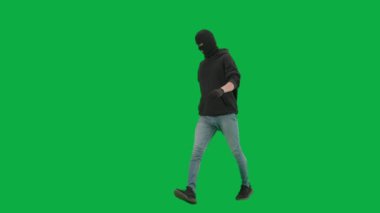 Soygun ve ceza konsepti. Krom anahtar yeşil ekrandaki hırsızın portresi. Kapüşonlu, kot pantolonlu ve kar maskeli bir adam suç işlemeye hazırlanıyor. Yarım dönüş.