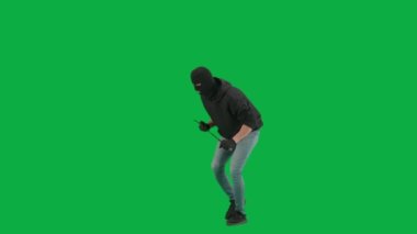 Soygun ve ceza konsepti. Krom anahtar yeşil ekrandaki hırsızın portresi. Kar maskeli ve kapüşonlu bir adam elinde levyeyle yürüyüp etrafa bakıyor. Yarım dönüş.