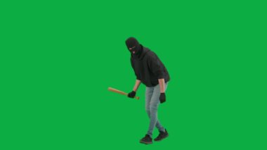 Soygun ve ceza konsepti. Krom anahtar yeşil ekrandaki hırsızın portresi. Kar maskeli ve kapüşonlu bir adam elinde beyzbol sopasıyla yürüyüp etrafa bakıyor. Yarım dönüş.