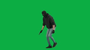 Soygun ve ceza konsepti. Krom anahtar yeşil ekrandaki hırsızın portresi. Kar maskeli ve kapüşonlu bir adam elinde silahla dolaşıyor. Etrafa bakıyor. Yarım dönüş.
