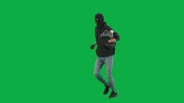 Soygun ve ceza konsepti. Krom anahtar yeşil ekrandaki hırsızın portresi. Kapüşonlu, kot pantolonlu ve kar maskeli bir adam para dolu bir çantayla polisten kaçıyor. Yarım dönüş.