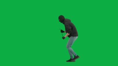 Soygun ve ceza konsepti. Krom anahtar yeşil ekrandaki hırsızın portresi. Kar maskeli ve kapüşonlu bir adam elinde levyeyle yürüyüp etrafa bakıyor. Yan görünüm