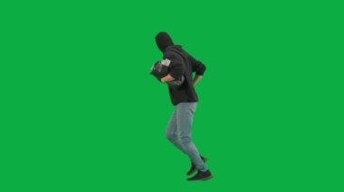 Soygun ve ceza konsepti. Krom anahtar yeşil ekrandaki hırsızın portresi. Kapüşonlu, kot pantolonlu ve kar maskeli bir adam para dolu bir çantayla polisten kaçıyor. Yan görünüm