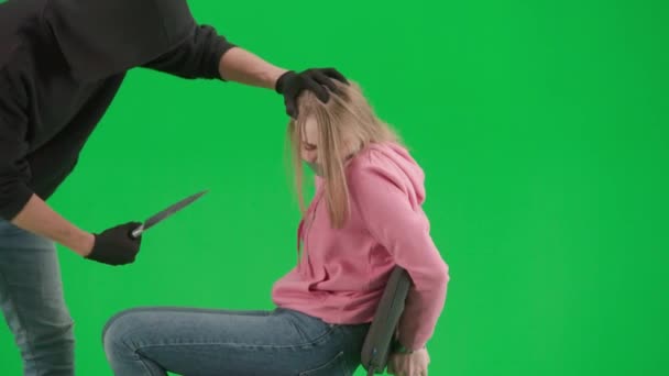 強盗と犯罪概念 クロマキーの緑色の背景に泥棒と犠牲者の肖像画 椅子に座っている少女は手を縛られ ナイフで盗まれた口の男は彼女を脅かします — ストック動画