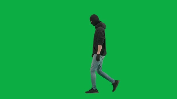 抢劫和犯罪概念 色键绿色屏幕背景上的小偷肖像 男子抢劫犯穿着帽衫 牛仔裤和黑色巴拉克拉瓦 步行准备犯罪 侧视图 — 图库视频影像