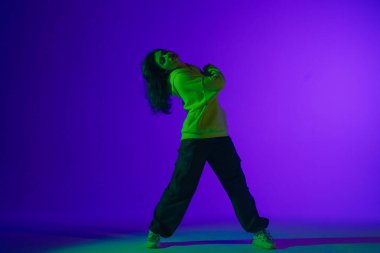 Stüdyoda canlı caz-funk performansı: günlük kıyafetlerle genç bir stil kız mor-yeşil ışık altında dansın ritmini ve enerjisini somutlaştırıyor
