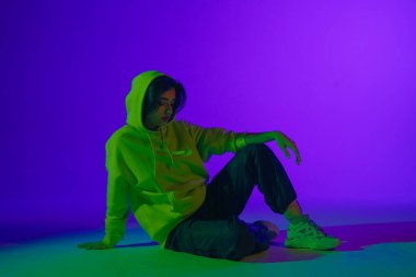 Stüdyoda canlı caz-funk performansı: günlük kıyafetlerle genç bir stil kız mor-yeşil ışık altında dansın ritmini ve enerjisini somutlaştırıyor