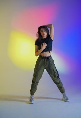 Siyah elbiseli genç kadın stüdyoda gradyan mavi, sarı, pembe neon ışıkla poz veriyor. Dansçı caz funk dansının unsurlarını gösteriyor. Çağdaş koreografi