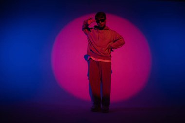 Stüdyoda mavi ışıkla hip hop dansı yapan günlük kıyafetli adam. Dansçı kırmızı ışık çemberinde ve vücut esnekliğini gösteriyor. Tam yükseklik. Modern sokak koreografisi