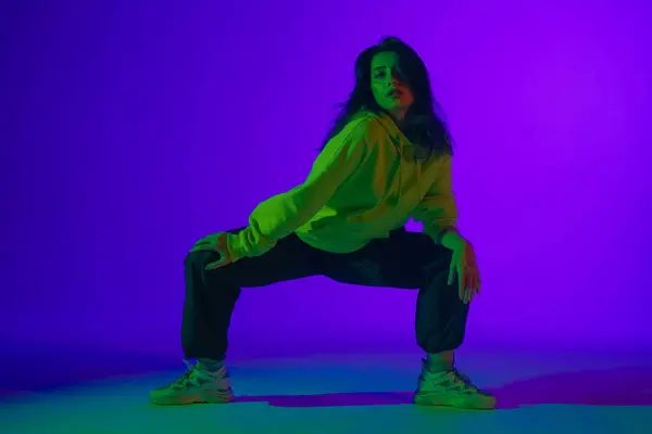 Live jazz-funk performance in the studio: a young stylish girl in casual clothes embodies the rhythm and energy of dance under purple-green light