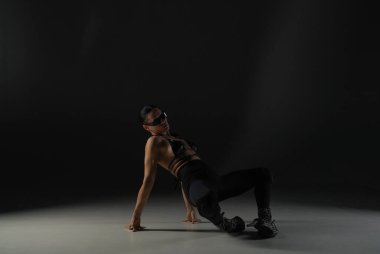 Siyah elbiseli genç bir kadın arka plandaki stüdyonun siyah arka planında poz veriyor. Dansçı yüksek topuklularla dans koreografisinin unsurlarını gösteriyor. Dans tanıtım çekimi konsepti