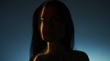 Vücut parçalarının güzelliği estetik yaratıcı konsept. Stüdyoda çekici bir kadın modelin portresi. Kadın silueti, parlak ışık huzmeleriyle, koyu ışık arka planında izole edilmiş, yakın görüntüye bakar..