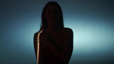 Güzellik vücudu estetik yaratıcı reklam konsepti. Stüdyoda kadın modelin portresi. Beyaz, düşük ışık arka planında poz veren çekici kadın silueti, seçici ışık huzmesi üzerinde hareket ediyor..