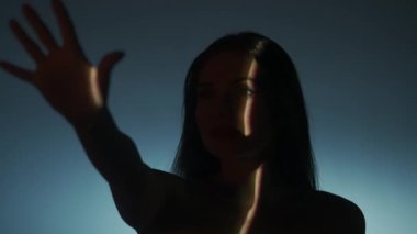 Güzellik vücudu estetik yaratıcı reklam konsepti. Stüdyoda kadın modelin portresi. Beyaz ışıklı arka planda çekici kadın yüzü silueti, kameraya gülümseyen ışık ışınlarına dokunmak.