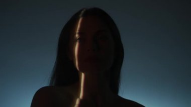 Güzellik vücudu estetik yaratıcı reklam konsepti. Stüdyoda kadın modelin portresi. Beyaz ışık arka planında poz veren çekici kadın silueti, yüzün üzerinde hareket eden seçici ışık hüzmesi.