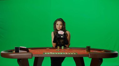 Kumarhane ve kumar ticari reklam konsepti. Stüdyoda krom anahtar yeşil ekranda zarif bir kadın. Blackjack poker masasında elinde kart hayranı siyah elbiseli çekici bir kadın..