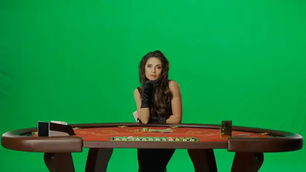 カジノとギャンブルの商業広告コンセプト クロマキーグリーンスクリーンのスタジオでエレガントな女性 ブラックジャックポーカーテーブルの黒いドレスで魅力的な女性がカメラを見ます — ストック写真