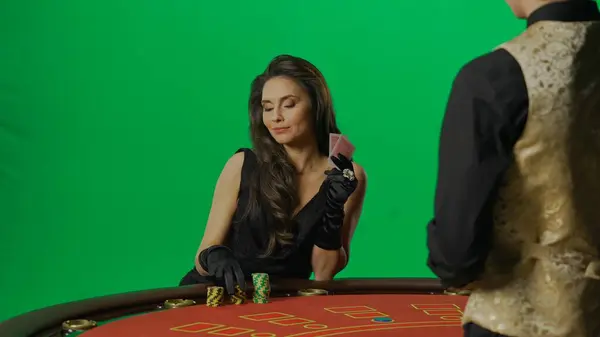 カジノとギャンブルの商業広告コンセプト クロマキーグリーンスクリーンのスタジオで豪華な女性 賭ける準備ができてブラックジャックポーカーテーブルでドレスと男のクロピエで女性を魅了 — ストック写真
