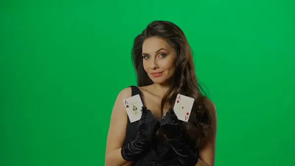 カジノとギャンブルの商業広告コンセプト クロマキーグリーンの背景にスタジオでエレガントな女性 カメラでエースカードのペアで黒いドレスで魅力的な女性 — ストック写真