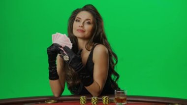 Kumarhane ve kumar yaratıcı reklam konsepti. Krom anahtar yeşil ekran yakından çekilmiş kadın portresi. Blackjack poker masasında oturan zarif kadın kartlarla poz veriyor, gülümsüyor. Yavaş çekim